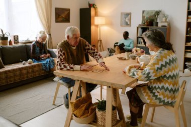 Arkadaşları kitap okurken ve tığ işi yaparken üst düzey bir çiftin domino oynadığı yüksek açı çekimi.