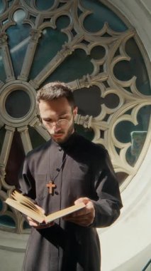 Siyah cüppeli genç bir papazın kutsal kitabı okuması ve kilise penceresinden gökyüzüne bakması dikey bir bakış.