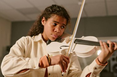 Orta ölçekte, çenesinin altında keman tutan Afrikalı Amerikalı genç kız stüdyoda yeni bir melodi yaratmaya çalışıyor.