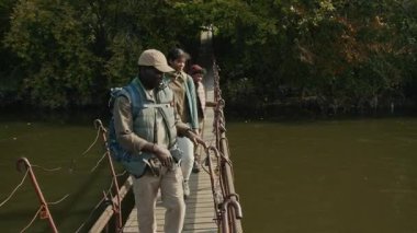 Baba, çocuklarına gittiği yeri gösterirken parmağıyla kampı işaret ediyor. Ailesinin sonbahar yürüyüşü sırasında nehir üzerinde asma yaya köprüsü boyunca ilerlemesi.