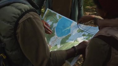 Üç turist bir günlük yürüyüş sırasında göl etrafında hangi yolu izleyeceklerine karar verirken bölge haritasını okuyorlar