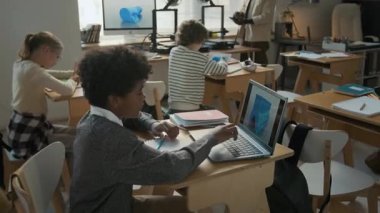 Genç öğrenciler görevleri üzerinde çalışırken, dizüstü bilgisayarlarında ve tabletlerinde 3D modele odaklanırken, Afro-Amerikan öğretmenler modern 3D modelleme sınıfında hos akıllı telefon kullanıyorlar.
