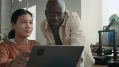 Dost canlısı Afrikalı Amerikalı erkek öğretmen öğrencisinin laptop ekranına bakıyor, okuldaki 3D modellik dersinde yardımcı olmaya çalışıyor.