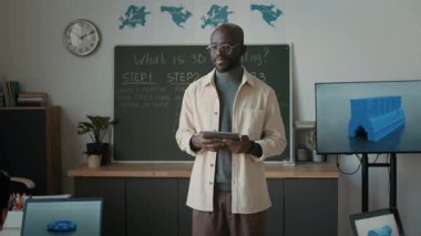 Afrika kökenli Amerikalı erkek öğretmenin genç öğrencilerine modern sınıfta 3D modellik yaptığını söylerken elde çekilmiş bir fotoğrafı.
