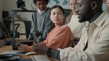 Genç öğrencilere 3 boyutlu modelleme ve baskı temellerini açıklayan Afro-Amerikan erkek öğretmen, modern okulda onun etrafını sardı.
