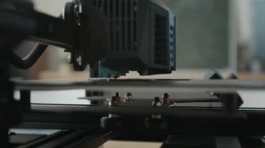 3D yazıcı ekstratörünün yakın plan çekimi, modern okuldaki baskı yatağına malzeme depoluyor.