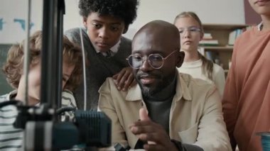 Afrika kökenli Amerikalı erkek öğretmen ve çocukların eğik çekimleri, okuldaki 3D modelleme dersi sırasında 3D yazdırılmayı beklerken bir araya geldi.