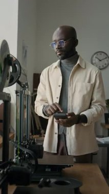 Modern okul sınıfındaki dokunmatik ekranı kullanarak, 3D yazıcı ayarlarından birini ayarlayan Afrikalı Amerikalı erkek öğretmenin dikey görüntüsü