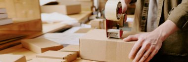 Kargo deposunda bant makinesiyle kutuları mühürleyen, teslimat için paketleri hazırlayan ve depo işlemleri sırasında çalışma alanını düzenleyen işçiler