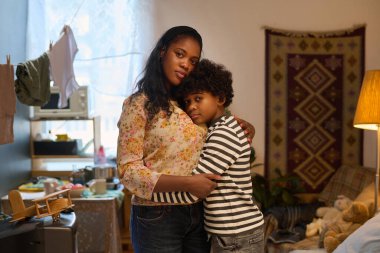 Portrait of mother lovingly embracing her child in a cozy living room setting with warm lighting and decorative elements creating homey atmosphere clipart