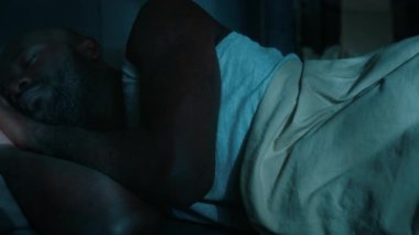 Afrika kökenli Amerikalı bir adamın gözleri kapalı gülümserken karısı geceleri yatakta yatarken ona arkadan sarılırken çekilen fotoğrafı.