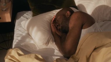 Afrika kökenli Amerikalı bir adamın sabah güneşli yatak odasında uyanmadan önceki son dakikalarında gülümserkenki yüksek açılı görüntüsü.