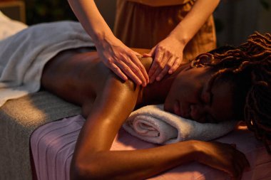 Orta ölçekli, tanınmayacak kadar narin bir kadın eli masaj yapan sevimli Afrikalı Amerikalı kadının omuzları.