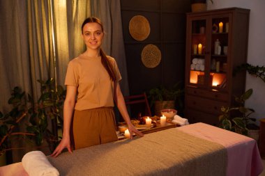 Kafkas masözünün yüksek açılı portresi masaj masasının yanında aroma mumları ve bitkilerle süslenmiş olarak duruyor.