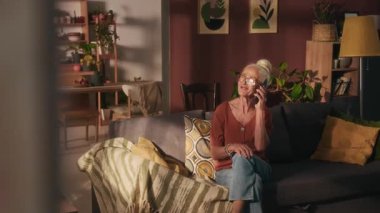 Bluz ve kot pantolon giymiş neşeli Kafkasyalı bayan koltukta otururken akrabalarıyla telefon görüşmesi yapıyor.