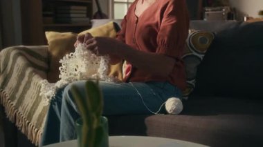 Beyaz iplik yumağıyla kanepede otururken, doğum günü hediyesi olarak örgü ören, gözlüklü, beyaz, yaşlı bir kadını yukarı kaldır.