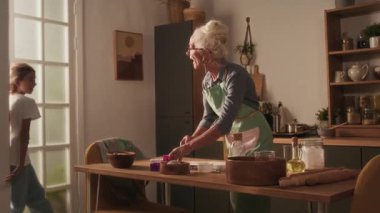 Mutfak masasını hazırlarken torunlarını görmekten mutlu olan büyükannelerine sarılmak için koşan iki kardeş.