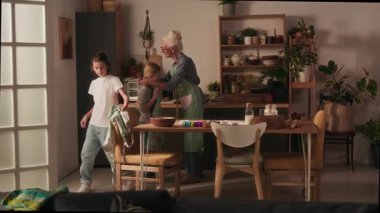 Büyükanne sandalyeden mutfak önlüğünü alıyor, torunu giydiriyor ve pişirmeye başlamadan önce torununa önlüğünü bağlamasında yardım ediyor.