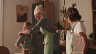 Gen alfa çocuk önlük giyiyor, neşeli büyükanne mutfakta birlikte yemek pişirmeden önce bir kıza yardım ediyor.