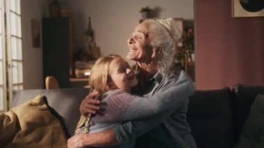 Mutlu bir büyükanne, sıcak bir oturma odasında, koltukta otururken neşeli bir alfa torununa sarılıyor.