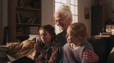 Neşeli bir büyükanne torunuyla sohbet ediyor. Torun kitabı tutarken ve kanepede dinlenirken onu okurken.