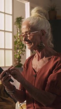 Kısa kollu bluz giymiş, yeni akıllı telefon kullanmayı öğrenirken arkadaşına mesaj gönderen yaşlı bir kadının dikey görüntüsü