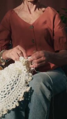 Evde yeni bir hobi edinirken beyaz iplikle örgü ören neşeli, beyaz iplik ören Kafkasyalı yaşlı kadının dikey görüntüsü