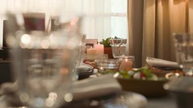 Zarif cam süslemeli yemek masası ve peçeteli tabaklar ve özel durumlar için özel olarak hazırlanmış mumlarla hafif aydınlatılmış.