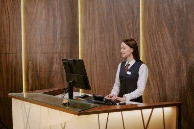 Güzel genç resepsiyonistin otel lobisinde çalışırken odayı kontrol etmek için bilgisayar kullanması geniş açı.