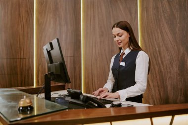 Genç beyaz resepsiyonistin otel lobisinde çalışırken klavyede daktilo kullanmasının geniş açılı görüntüsü.