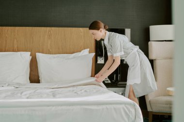 Büyük boy boncuklu geniş bir otel odası ve misafirler için battaniye hazırlayan genç bir kadın.