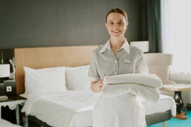 Otel odasında fotoğraf çektirirken elinde havlu tutan gülümseyen hizmetçi portresi.