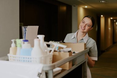 Yetişkin, beyaz bir hizmetçinin el arabasını deterjanlar, temiz havlular ve çarşaflarla ittiği orta boy bir çekim.