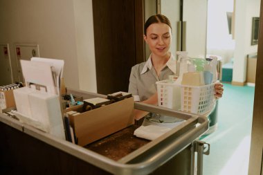 Gülümseyen beyaz bir hizmetçinin el arabasından farklı deterjanlar aldığı yüksek açılı bir fotoğraf.