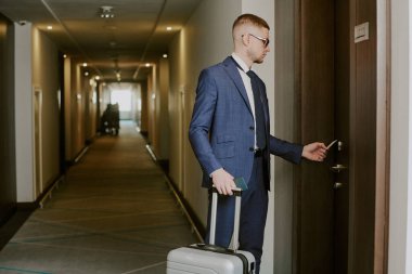 Kapıda duran gümüş bavullu adamın, otel odasını açmak için kart kullanırken çekilmiş bir fotoğrafı.