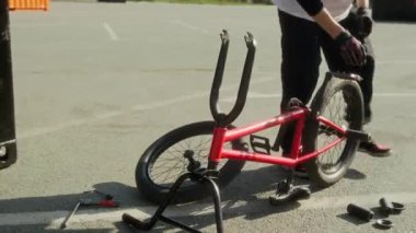 Genç BMX sürücüsü kaykay parkındaki asfaltta parçalanmış parçalarla bisikleti tamir ederken tekerlek ve mandalları ayarlamak için araçlar kullanıyor