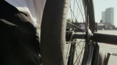 BMX sürücünün eldivenli ellerini yakın çekim. Mandal ve dingili aletle sıkılaştırma. Sonra da kaykay parkında bisiklet sürerken dönme dolap.