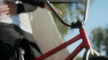 BMX sürücüsünün gidona dönüşünü, barspin tekniğini, yaz günü kaykay pistinin yanında bisikletle hareketsiz duruşunu yakından izle.