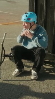 Genç BMX sürücüsünün koruyucu kask takıp, şehir kaykay parkında antrenman yapmadan önce arkadaşlarıyla birlikte ayağa kalkıp bisiklet sürerken dikey çekimi.