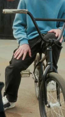 Genç BMX sürücüsünün günlük kıyafetleri ve koruyucu kasklarıyla bisikletle dışarıda antrenman yaparken arkadaşlarıyla sohbet ederken dikey çekimleri.