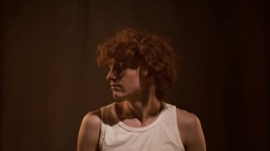 Beyaz askılı beyaz tişörtlü bir gencin göğsünden yukarı doğru başı sağa sola dönük saçlarına dokunup çığlık atarken.