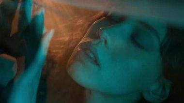Sakin genç bir kadının aşırı yakın plan görüntüsü. Şeffaf bir elbiseye dokunuyor, gözleri kapalı ve yavaşça başını hareket ettiriyor.