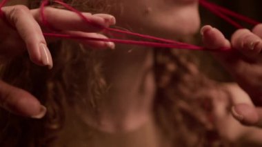 Kafkasyalı genç bir kadının beyaz manikürlü narin parmaklarının yakın plan görüntüsü başını kaplayan kırmızı ipliklere dokunuyor.