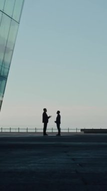 Çatıda dikilen ve iş projesini özel olarak tartışan iki tanınmayan iş adamının dikey çekimi.