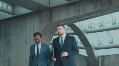 Keskin giyimli iki iş adamının modern iş merkezlerinde gezinirken düşük açılı çekimleri izlemek ve iş hakkında konuşmak.