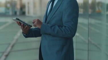 Gözlüklü Afro-Amerikan bir adamın açık havada dikilip dijital tabletine sarılmış görüntüsü.