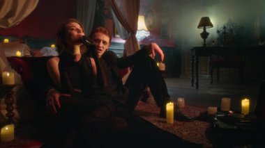 Vampir kadın ve siyahlı adam mataradan sırayla içerken loş ışıklı yatak odasında titreşen mum ışığında birbirine yakın oturuyorlar.