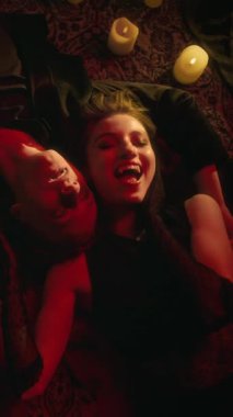 Vampir çiftin mum ışığında yan yana yatıp gülümserkenki dikey görüntüsü.