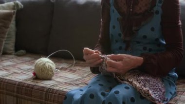 Gözlüklü yaşlı kadının oturma odasında kanepede oturup iplik ve kancayla örgü örüşünü çek.