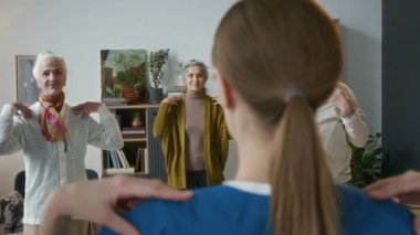 Bakıcının bakım evinde grup fitness seansı sırasında hafif egzersiz yapmasını izleyen çeşitli yaşlı insanlar